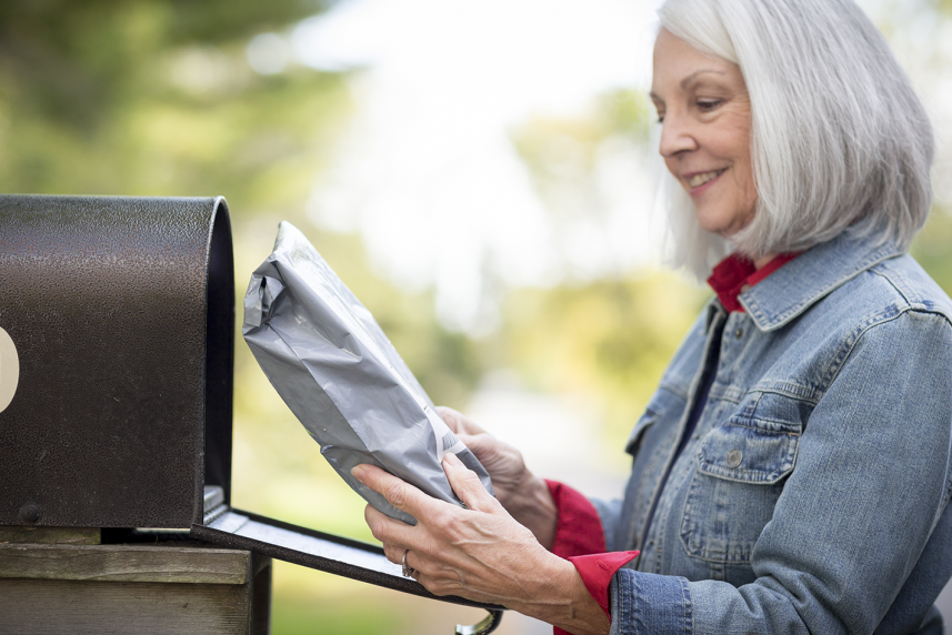 Older woman taking package out of mailbox for article on health insurance benefits